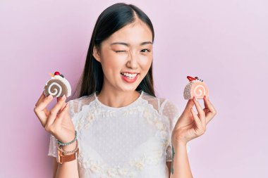 Genç Çinli kadın elinde pasta tatlısı ile kameraya bakıyor. Seksi bir ifadeyle, neşeli ve mutlu bir yüzle.. 