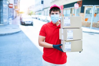 Coronavirus koruması takan beyaz bir kurye elinde karton paketler, şehirde yürüyor..