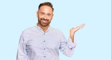 Yakışıklı, orta yaşlı, iş gömleği giyen, neşeli bir şekilde gülümseyen ve avuç içi kameraya bakan bir adam.. 