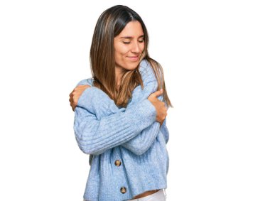 Gündelik kıyafetler giyen, mutlu ve olumlu bir şekilde kendine sarılan, kendinden emin gülümseyen genç bir kadın. Sevgi ve özgüven. 