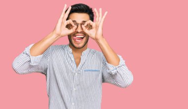 Genç, yakışıklı, sıradan kıyafetler ve gözlük takan dürbün gibi jest yapan, gözleri parmaklarından bakan bir adam. çılgın ifade. 