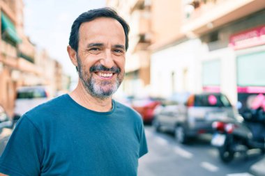 Orta yaşlı, sakallı, açık havada mutlu gülümseyen bir adam.