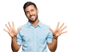 Yakışıklı İspanyol adam gündelik giysiler giyip on numarayı gösterip işaret ederken kendinden emin ve mutlu bir şekilde gülümsüyor.. 