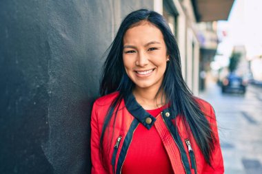 Genç Latin kadın gülümsüyor. Şehrin duvarına yaslanmaktan mutlu..