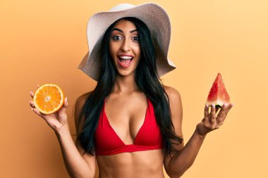 Güzel İspanyol kadın karpuz yiyor ve turuncu kutlama yapıyor. Çılgınca ve şaşkınlık içinde gözleri açık heyecanla haykırıyor.. 