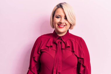 Genç, güzel, sarışın ve cüsseli bir kadın izole pembe arka planda günlük gömlek giyiyor ve yüzünde mutlu ve havalı bir gülümseme var. Şanslı kişi..