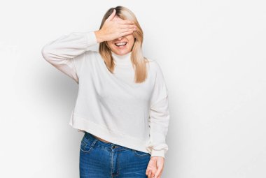 Sıradan bir kazak giyen, gülümseyen ve gülen genç, beyaz bir kadın şaşkınlık için gözlerini kapatıyor. kör kavram. 