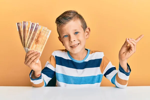 愛らしいCaucasian子供を保持500ノルウェークローネ紙幣上に座っテーブル笑顔幸せなポインティングで手と指で側面に — ストック写真