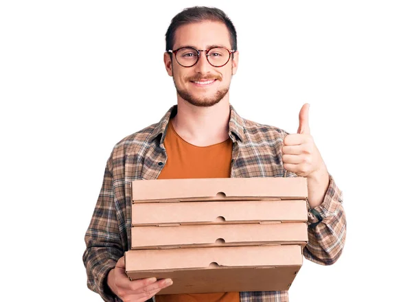 年轻英俊的高加索男子拿着送披萨盒 面带微笑 面带微笑 大拇指向上做得很出色 并签了字 — 图库照片