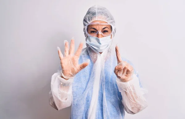 白い背景の上に保護コロナウイルス装置を身に着けている中年の看護師の女性が現れ 自信と幸せ笑顔ながら指番号6で指摘します — ストック写真
