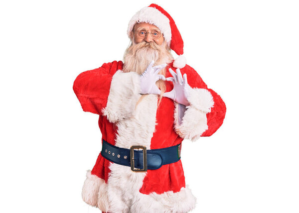 Old senior man with grey hair and long beard wearing traditional santa claus costume smiling in love doing heart symbol shape with hands. romantic concept. 