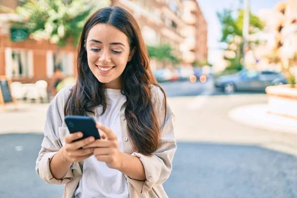 Genç İspanyol kadın şehirde akıllı telefon kullanarak mutlu bir şekilde gülümsüyor..