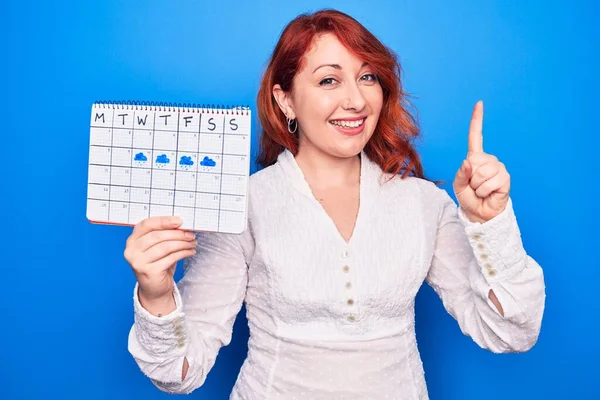 Jovem Ruiva Segurando Calendário Meteorológico Mostrando Semana Chuvosa Sobre Fundo — Fotografia de Stock