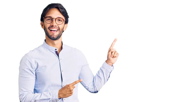 ビジネスシャツと眼鏡を身に着けているハンサムなヒスパニック系の男笑顔とカメラを見て2本の手と指で側面を指して — ストック写真