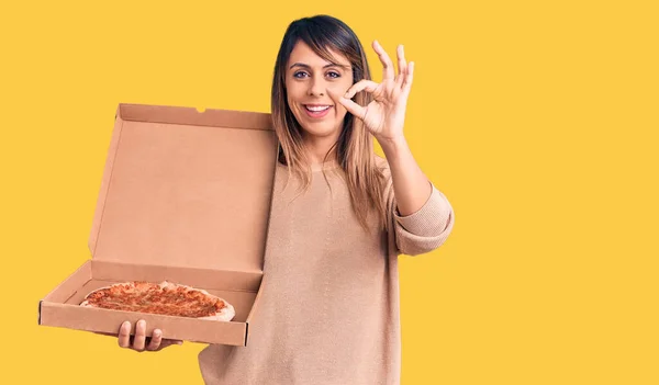 年轻而漂亮的女人拿着装有披萨的纸盒 手拿着手签 微笑着表示友善的手势 是极好的象征 — 图库照片