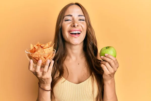 年轻的黑发女人拿着玉米片和健康的绿色苹果笑着大声笑着 因为有趣的疯狂笑话 — 图库照片