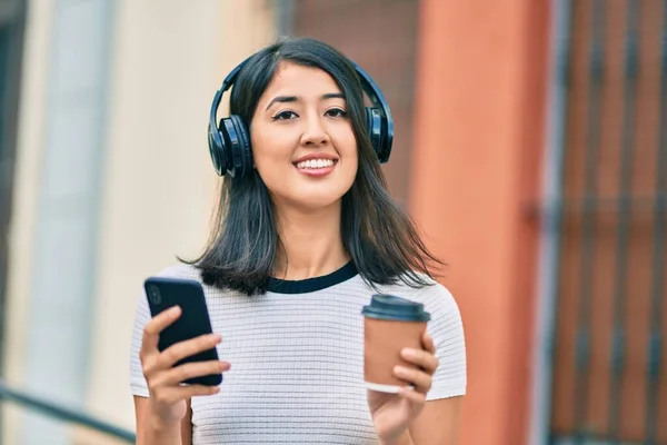 若いヒスパニック女性はコーヒーを飲み 市内でスマートフォンやヘッドフォンを使用しています — ストック写真