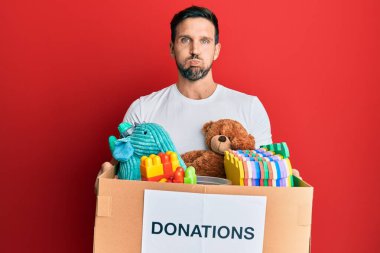 Genç yakışıklı adam, elinde oyuncak kutusuyla komik suratlı, şişen yanakları olan bir bağış kutusu tutuyor. Ağzı havayla şişer, havayı yakalar.. 