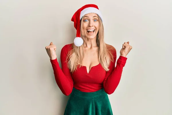 美丽的高加索女人 身穿圣诞服装 头戴圣诞礼帽 高举双臂 睁大眼睛 为成功感到惊奇和惊奇 获奖者概念 — 图库照片