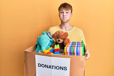 Kafkasyalı genç bir adam, elinde oyuncak kutusuyla komik suratlı, şişen yanakları olan bir bağış kutusu tutuyor. Ağzı havayla şişer, havayı yakalar.. 