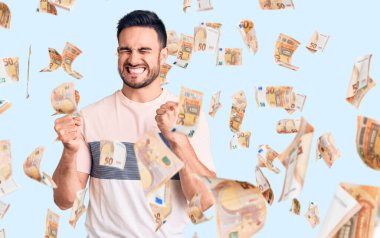 Başarılı olmak için heyecanlı, kolları havada ve gözleri kapalı gülümseyerek zaferi kutlayan gündelik giysiler giyen genç yakışıklı bir adam. Kazanan konsept.