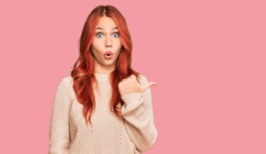 Kış süveteri giyen genç, kızıl saçlı bir kadın elleri yana dönük, ağzı açık, şaşkın bir ifadeyle şaşırdı.. 