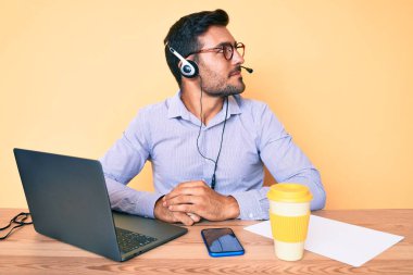 Çağrı merkezindeki operatör kulaklığı takmış genç İspanyol adam yan tarafa bakıyor, rahat profil pozu veriyor kendine güveni tam bir gülümsemeyle.. 