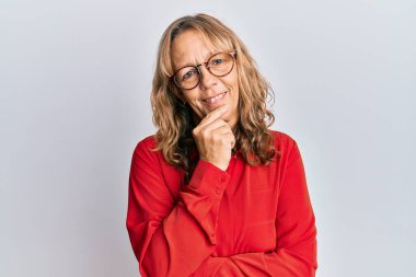 Orta yaşlı, sarışın, sıradan kıyafetler ve gözlük takan, gülümseyen kolları çapraz ve çenesi açık kameraya bakan bir kadın. Olumlu düşünmek. 