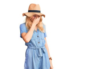 Genç, sarışın, yaz şapkası ve elbisesi giyen, burnu ve gözleri ovuşturmaktan yorgun düşmüş yorgun ve başı ağrıyan bir kadın. Stres ve hüsran kavramı. 