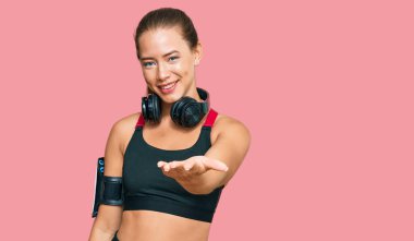 Güzel sarışın kadın spor kıyafetleri giyiyor ve kulaklık takıyor. Gülümsüyor. Avuç içi dolusu yardım ve kabullenme sunuyor.. 