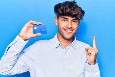 Elinde kredi kartı tutan genç İspanyol adam mutlu bir şekilde elini ve parmağını kenarda gezdiriyor. 