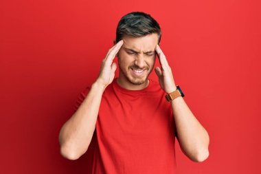 Yakışıklı, beyaz bir adam, günlük kırmızı tişört giyiyor, eli başının üstünde, stresten baş ağrısı çekiyor. migren ağrısı. 