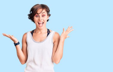 Kısa saçlı, spor kıyafetleri giyen güzel bir kadın zaferi mutlu bir gülümsemeyle kutluyor ve ellerini kaldırarak kazanan bir ifade sergiliyor. 