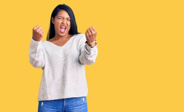 Uzun saçlı, günlük kıyafetler giyen, kızgın, kızgın, yumruklarını kaldıran öfkeli, öfkeyle bağıran İspanyol bir kadın. öfke ve agresif konsept. 