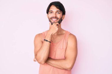 Yakışıklı, sıradan kıyafetler giyen, kameraya kendinden emin, kollarını kavuşturmuş ve çenesini kaldırmış, gülümseyen bir İspanyol. Olumlu düşünmek. 