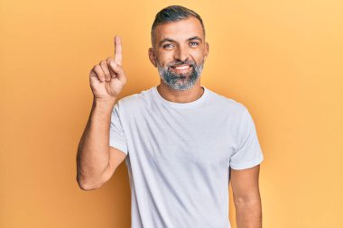 Orta yaşlı beyaz tişört giyen yakışıklı bir numaralı parmağını gösterip onu gösterirken kendinden emin ve mutlu bir şekilde gülümsüyor.. 