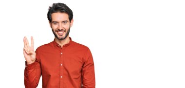 Gündelik kıyafetler giyen genç İspanyol adam üç numarayı gösterip işaret ederken kendinden emin ve mutlu gülümsüyor.. 