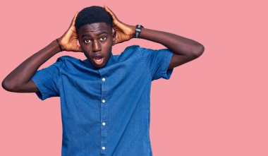 Genç Afrikalı Amerikalı sıradan kıyafetler giyen çılgın ve elleri başında korkmuş ağzı açık bir şekilde şok geçirmekten korkan ve şaşıran bir adam. 