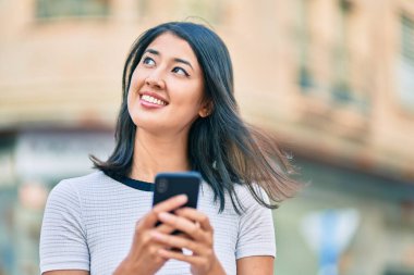 Genç İspanyol kadın şehirde akıllı telefon kullanarak mutlu bir şekilde gülümsüyor..