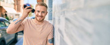 Genç İrlandalı gülümseyen mutlu bir adam şehrin caddesinde akıllı telefonda konuşuyor..