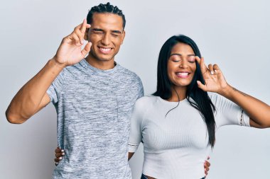 Gündelik giysiler giyen genç Latin çift umut ve gözlerin kapalı bir şekilde parmaklarını çaprazlayarak gülümsüyor. Şans ve batıl inançlar. 