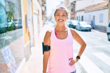 Şehirdeki orta yaşlı sporcu kadın gülümseyerek antrenman yapıyor.