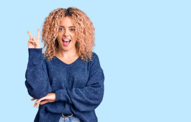 Kıvırcık saçlı, sıradan bir kazak giyen, kameraya gülümseyen ve parmaklarıyla zafer işareti yapan genç sarışın kadın. İki numara.. 