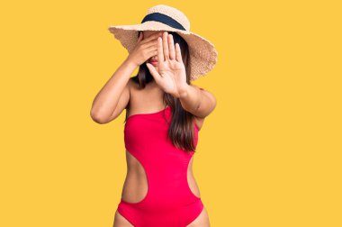 Mayo ve yaz şapkası takan genç ve güzel bir Latin kız ellerle gözlerini kapatıyor ve üzgün ve korku ifadeleriyle jest yapıyor. utangaç ve olumsuz kavram. 
