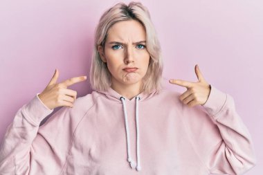 Genç sarışın kız parmakları kuşkucu ve gergin olan ağzı işaret ediyor, sorun yüzünden kaşlarını çatıyor. negatif kişi. 