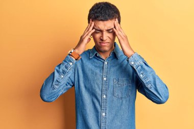 Genç Afro-Amerikan bir adam, elleri başının üstünde, günlük kıyafetler giyiyor, stres yüzünden baş ağrısı çekiyor. migren ağrısı. 