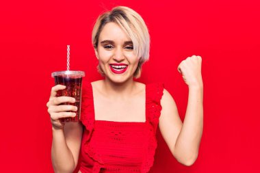 Genç, güzel, sarışın bir kadın bir bardak kola içiyor gururla bağırıyor, zaferi kutluyor ve kollarını kaldırarak başarıyı kutluyor. 