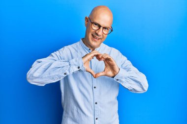 Orta yaşlı, kel, sıradan kıyafetler ve gözlük takan, aşkta gülümseyen, elleriyle kalp sembolü yapan bir adam. romantik kavram. 