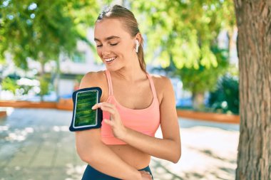 Genç sarışın sporcu. Parkta egzersiz yaparken kulaklık takıyor.