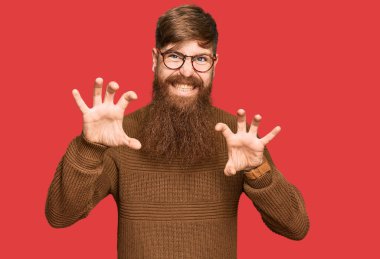 Genç İrlandalı kızıl elbiseli ve gözlüklü bir adam komik bir şekilde gülümsüyor kedi gibi pençe hareketi yapıyor, agresif ve seksi bir ifade. 